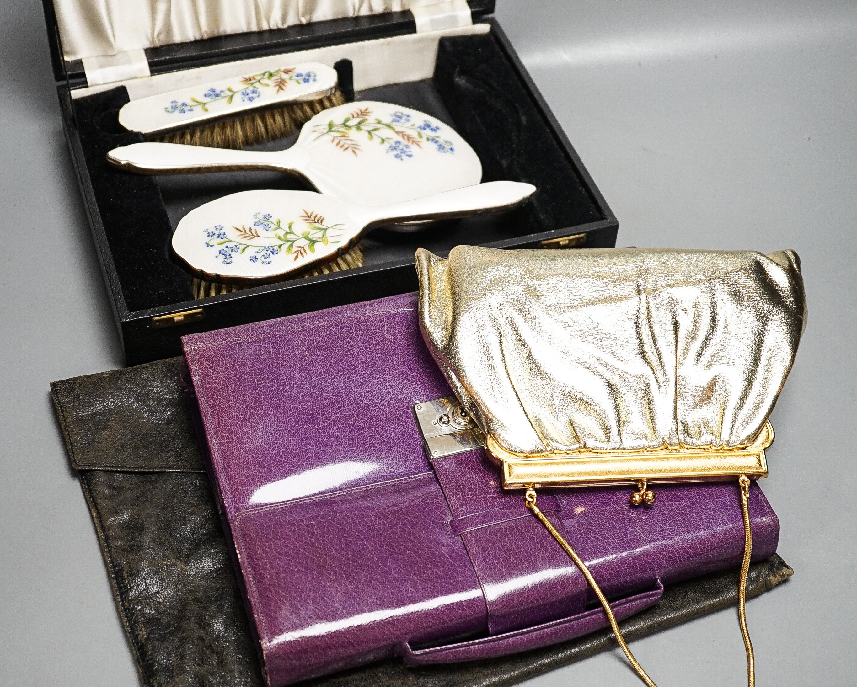 A boxed, three piece silver plated translucent enamelled dressing set, a purple leather stationary case and an evening bag